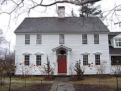 A white wooden house with no shutters, roof, and central chimney, and trees around