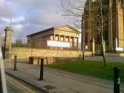 A small classical temple-like style building in the shadow of the cathedral