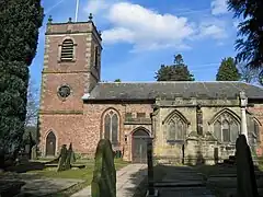 A church with a brick Neoclassical tower and body and a stone Gothic chapel protruding in the foreground