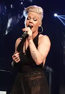 A blonde woman wearing a black dress and singing into a microphone