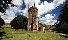 Stone building with square tower. In the foreground is a grassy area with gravestones.