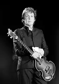 A man wearing a dark suit, holding a bass guitar