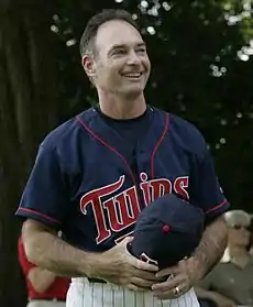 A smiling man wearing a navy-blue baseball jersey with "Twins" across the chest in red script