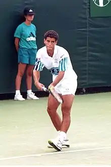 A man, with a modern racket in his right hand and a tennis ball in his left hand, prepares to serve