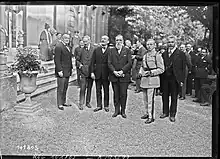 black and white photograph of six men in front of a crowd at the foot of a staircase on the left.