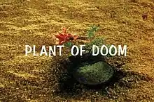 The image shows a plant with sand around it. The plant has a single flower and the words "Plant of Doom" superimposed over it.