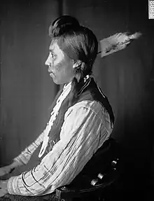 A Yakama man's face in profile, facing left. He is wearing a mix of native and western clothing, with a feather in his hair.