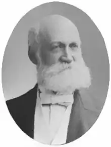 A black-and-white portrait of Charles Edward Warburton, an older Caucasian man with a bushy white beard and dressed in white-tie attire.