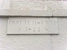 A white wall carries a stone plaque engraved with the word "Pottersfield" in upper case letters. Below this are the numerals "1822".