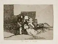 Huddled behind the ruins of a building, two women, one with a child in her arms, lay a third to her permanent rest in the ground. To the rear, another woman lies dead.