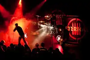 Project 86 performs at a concert. The entire band plays on a stage engulfed in red lights.