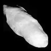 An irregularly shaped oblong body is fully illuminated. It is elongated in the direction from the top left to bottom left. Its surface is covered by craters.