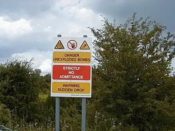 Sign warning of unexploded munitions and hazard posed by the crater