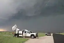 A large radar dish mounted on a white pickup truck scans the dark, cloudy sky.