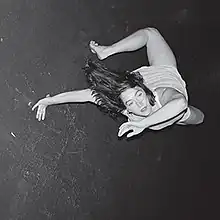 A 90 degrees rotated grayscale photo of a woman doing the bridge exercise, standing on her both feet and one hand, with her torso being rotated, and her second hand brought next to her face.