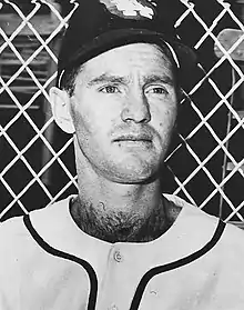 A man in a white baseball uniform and dark cap.