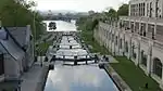 A small canal with a set of locks leading from a river near a large city.