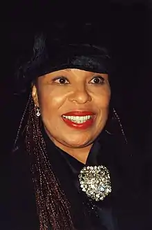 A dark-skinned woman with long braided hair, smiling broadly