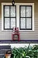 A lonely red chair decorated with Mardi Gras beads sits on a porch.