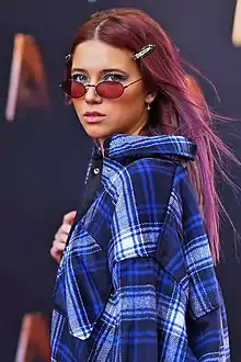 A woman wearing a plaid coat and sunglasses at an awards event.