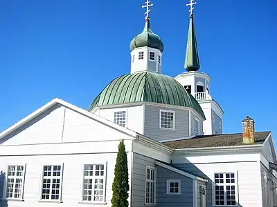 alt=Photograph of St. Michael's Cathedral in the sunlight, with bright white walls and green domes and spires reaching to the sky.