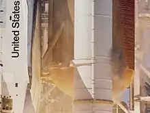 The Space Shuttle immediately following liftoff, from the viewpoint near the right SRB. Gray smoke is apparent around the SRB.