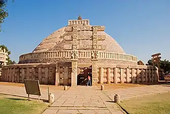 A large stupa in stone with an elaborate gate in front