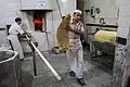 Inside the bakery, one person is baking and another is delivering bread.