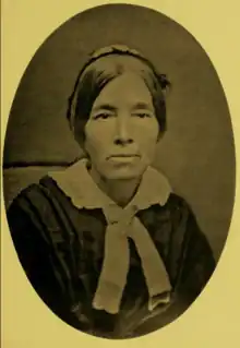 B&W oval portrait photo of a middle-aged woman with her hair in an up-do, wearing a dark shirt with a white collar.