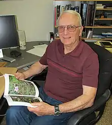 man seated in chair at desk, holding a book about mangroves