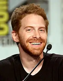 A smiling bearded man sitting in front of a microphone