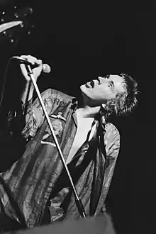 Black-and-white photo of a spiky-haired youth singing into a microphone