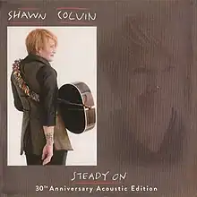 A photo of Colvin from behind with an acoustic guitar slung around her body