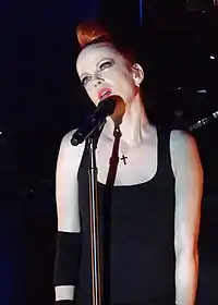 A light-skinned woman with red hair is seen looking up while she sings into her microphone