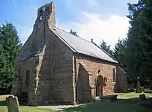 A small stone church with a Norman doorway and a double bellcote