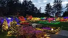 View west across the garden from the pavilion showing the southern half. Walkways and plants are decorated with holiday lights.