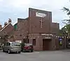 A brick building with an angular façade consisting of stepped brick walls above an entrance porch with a wooden door in a recess. A crucifix and the words "SHOREHAM FREE CHURCH" are on the façade.