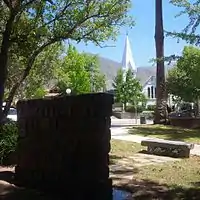 Sierra Madre Memorial Park at Sierra Madre Blvd and Hermosa looking North. From foreground to background: Weeping Wall Veterans Memorial, Sierra Madre Veterans Time Capsule bench, 1905 World War I Cannon,  Sierra Madre Boulevard, The Old North Church and the San Gabriel Mountains