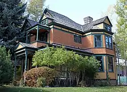 A large wooden house, yellow and orange with green trim and many projecting gables