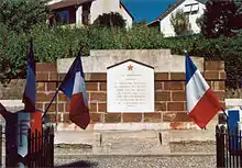 A low red brick memorial topped with a red star and flanked by French flags