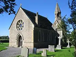 Stone building with small tower attached to the right hand side. At the nearest end is a circular window above an arched doorway.