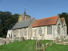 A stone church seen from the southeast. Nearest is the chancel with a red tiled roof, beyond that is the larger nave, with a slate roof, and at the west end is a tower with a spirelet