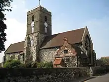 A stone church with a central tower, red tiled roofs, and a protruding vestry with a Dutch gable