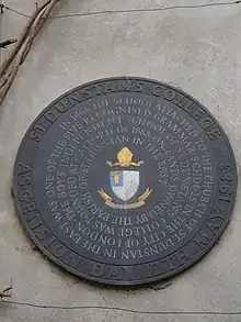 Roundel plaque bearing the college arms with spiral inscription reading "In 1466 the school attached to St Dunstan in the East was one of five recognised grammar schools in the City of London • The boys independent school St Dunstan's College was founded at Catford in 1888 on lands owned by St Dunstan in the East"