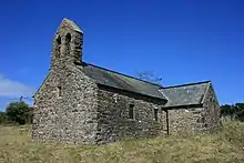 A simple stone church with a slate roof, a bellcote on the nearest gable and a transept on the right