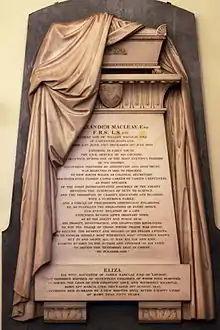 Photograph of a marble memorial on a wall with carved fabric draped over it and text on a panel