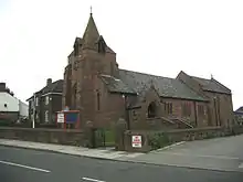 A stone church with squat west tower topped by a short broach spire