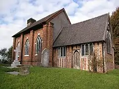 A church with a brick nave on the left, and a smaller timber-framed chancel on the right