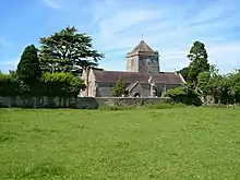 Gray stone building with arched windows. A central tower has a clock on the near face and is surmounted by a weather vane.