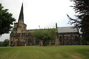 A stone Gothic church with a tower on the left capped by a recessed spire